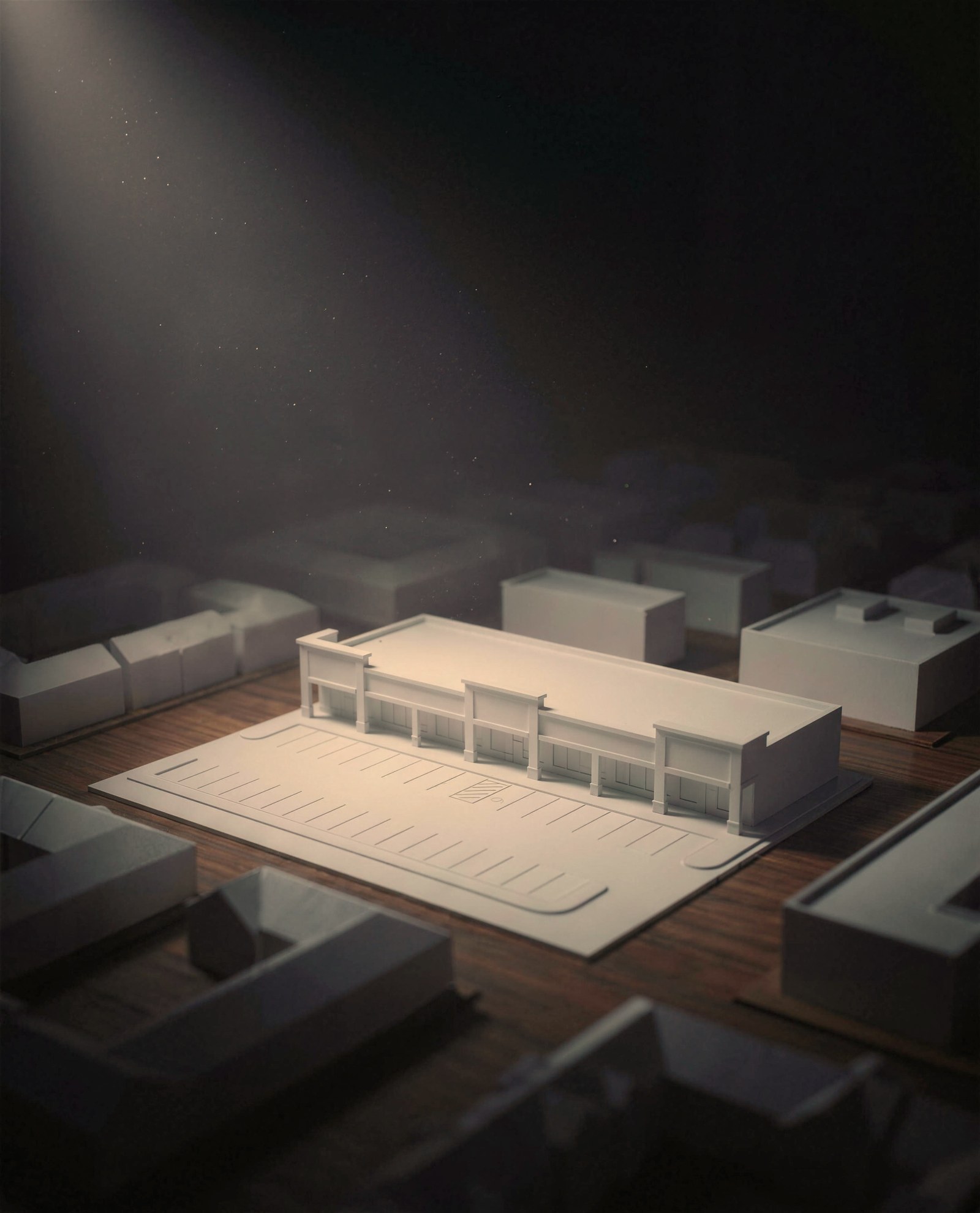 A white architectural model of a retail strip center and parking lot under a single spotlight